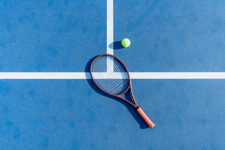 High-angle view of tennis racket and ball on blue court surface iStock