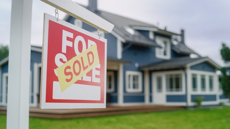 Close Up of a House Sold Sign on a Lawn in Front of a Big Modern House with Traditional Architecture. Housing Market Concept with Residential Property in the Countryside. iStock